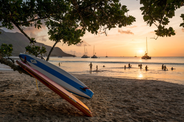 Photo of a beautiful sunset scene in Seychelles - kayaks, beach and swimming people. Buy a canvas, framed or acrylic fine art print.