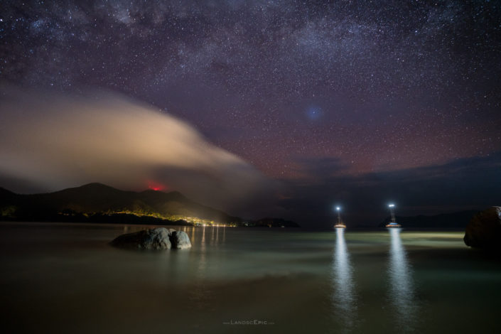 Photo of a Milky Way peaking out of clouds over beach in Seychelles. Buy a canvas, framed or acrylic fine art print.